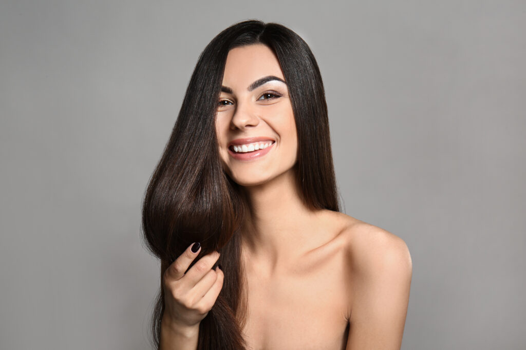 Portrait of beautiful young woman with healthy long hair on grey background